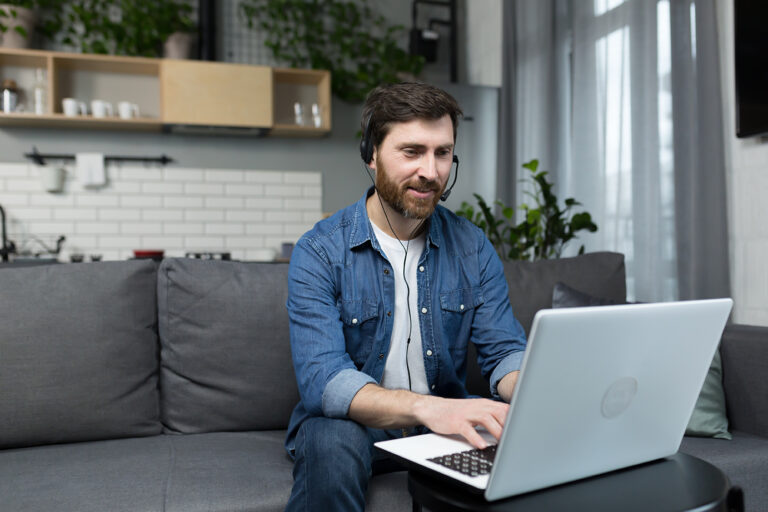 Person comfortably attending a mental health awareness session online while seated on a sofa with a computer and headset.